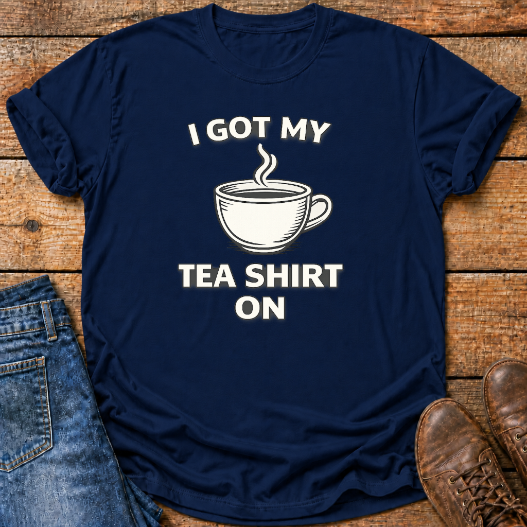 A navy blue graphic t-shirt with the white text 'I GOT MY TEA SHIRT ON' and a white teacup illustration, styled in a flat lay on a rustic wooden background with jeans and brown shoes.