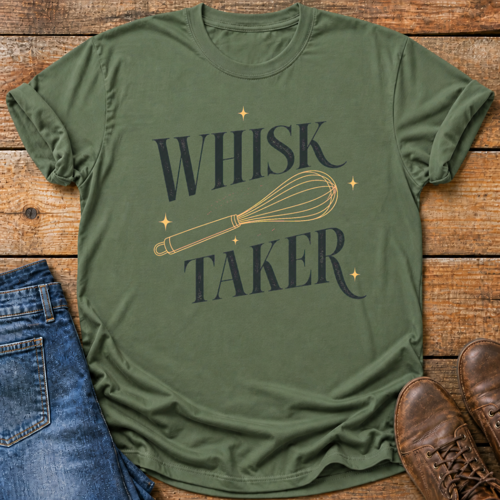 An olive green graphic t-shirt laid flat on a rustic wooden background, styled with blue jeans and brown leather shoes. The t-shirt features a dark navy blue graphic that reads 'WHISK TAKER' with a gold-colored whisk illustration and small gold stars.