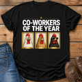 A black graphic t-shirt laid flat on a rustic wooden surface, styled with blue jeans on the left and brown leather shoes on the right. The t-shirt features the text 'CO-WORKERS OF THE YEAR' above three cartoon chicken portraits with gold frames.