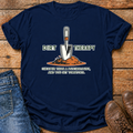 A navy blue graphic t-shirt laid flat on a rustic wooden surface, styled with blue jeans on the left and brown leather shoes on the right. The t-shirt features a graphic of a gardening trowel in a pile of dirt with the text 'DIRT THERAPY' and 'CHEAPER THAN A PSYCHOLOGIST, AND YOU GET TOMATOES.