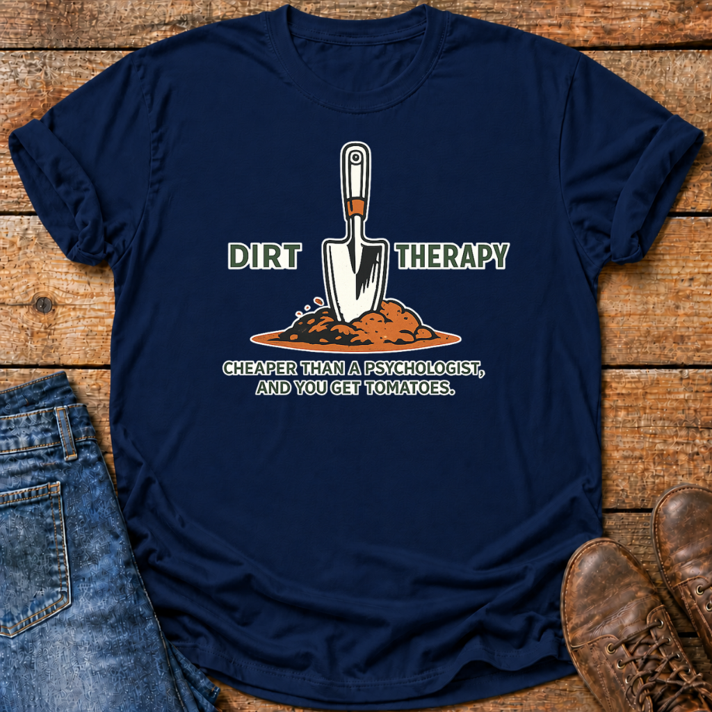 A navy blue graphic t-shirt laid flat on a rustic wooden surface, styled with blue jeans on the left and brown leather shoes on the right. The t-shirt features a graphic of a gardening trowel in a pile of dirt with the text 'DIRT THERAPY' and 'CHEAPER THAN A PSYCHOLOGIST, AND YOU GET TOMATOES.