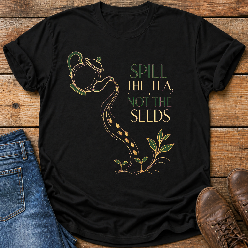 A black short-sleeve graphic T-shirt laid flat on a rustic wooden surface, styled with blue jeans and brown shoes. The shirt features a printed design of a teapot pouring tea into seed pods that grow into small plants, with the text 'SPILL THE TEA, NOT THE SEEDS' in green and gold lettering.