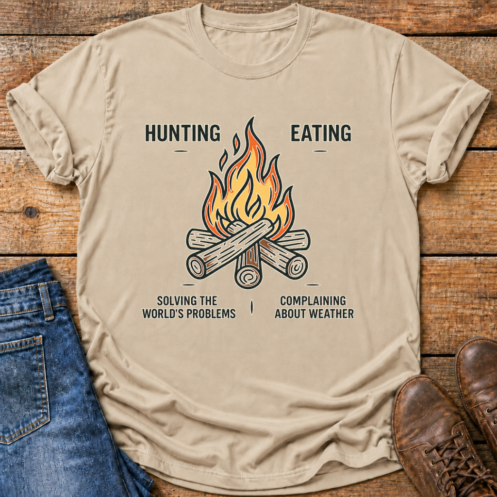 A beige graphic t-shirt laid flat on a rustic wooden background, styled with blue jeans and brown leather shoes. The t-shirt features a graphic of a campfire with the text 'HUNTING EATING' above and 'SOLVING THE WORLD'S PROBLEMS COMPLAINING ABOUT WEATHER' below.