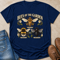 A navy blue graphic t-shirt featuring illustrations of three bees (honeybee, bumblebee, carpenter bee) and the text 'BEES OF THE GARDEN'. The shirt is styled in a flat-lay arrangement on a beige surface alongside blue jeans and brown leather boots.
