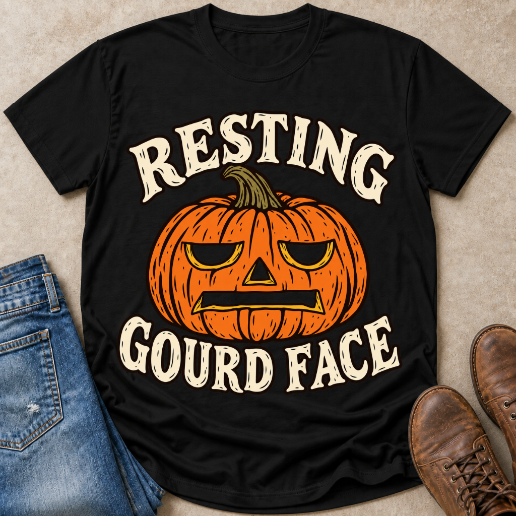 An black graphic t-shirt featuring a carved orange pumpkin and the text 'Resting Gourd Face' in a rustic cream font, styled in a flat-lay with blue jeans and brown boots on a beige background.