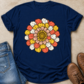 A navy blue short-sleeve t-shirt with a large retro-style zennia flower graphic on the chest, styled in a flat-lay with blue jeans and brown leather boots on a beige textured background.